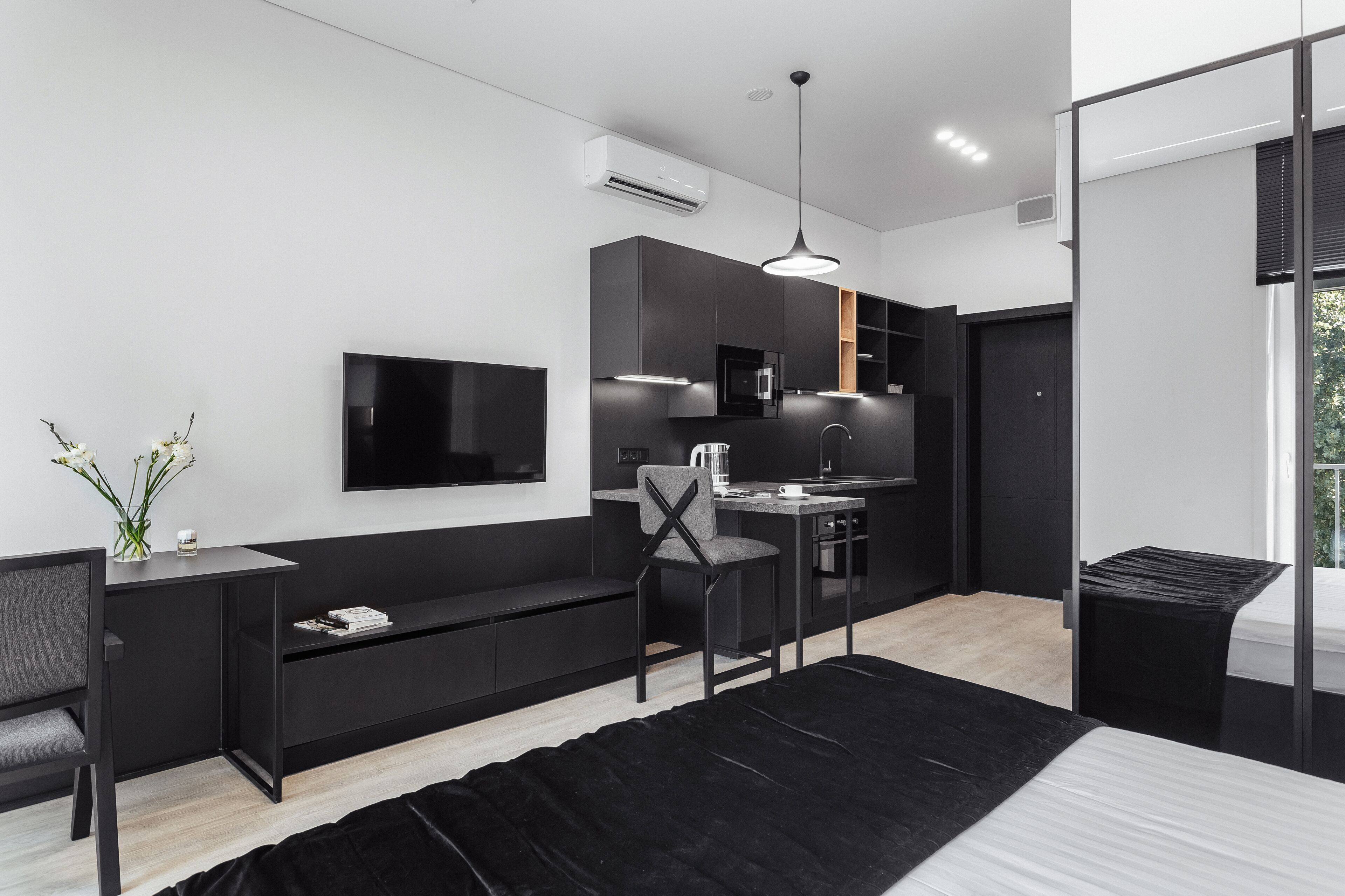 Un espacio habitable moderno y funcional, con una decoración en blanco y negro, televisor de pantalla plana, kitchenette y un gran ventanal.