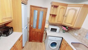 A compact kitchen with wooden cabinets, a washing machine, a microwave, and a toaster. - Garfield Villa-beautiful 4-bed House in Gillingham (Gillingham)