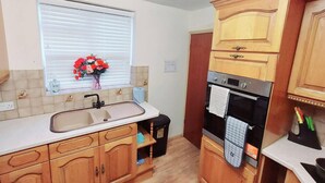A kitchen with wooden cabinets, a sink, a window with blinds, and a vase with flowers. - Garfield Villa-beautiful 4-bed House in Gillingham (Gillingham)
