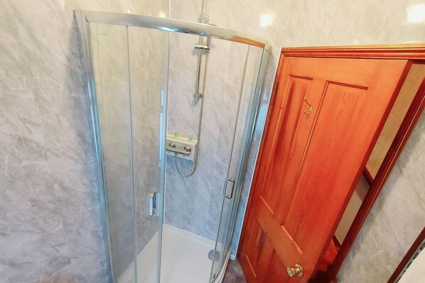 A bathroom with a glass shower enclosure, a wooden door, and a marble wall.