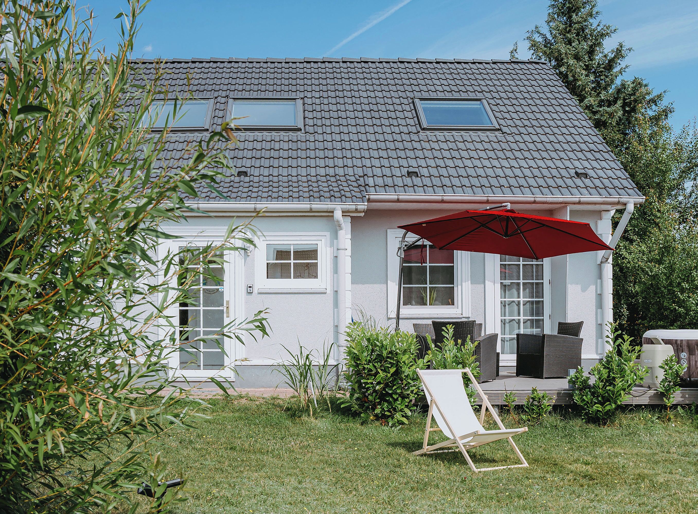 A house with a tiled roof, a red umbrella, and a lawn chair.