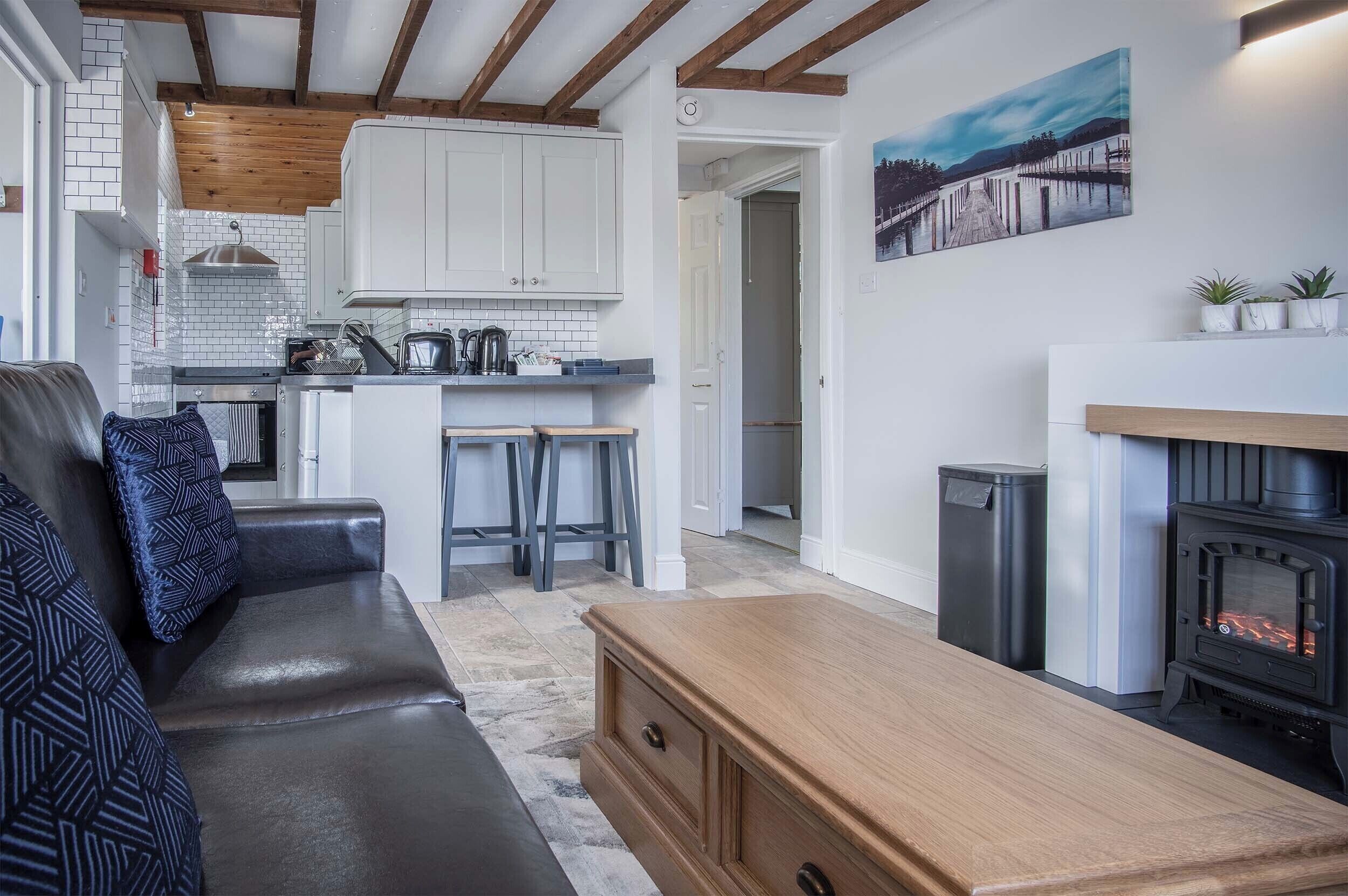 A cozy living area with a sofa, a wooden table, a fireplace, and a kitchen in the background.