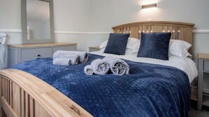 A neatly made bed with a blue blanket, two pillows, and rolled towels on a wooden headboard. - Honeysuckle Cottage - 1 Bedroom - Amroth (Narberth)