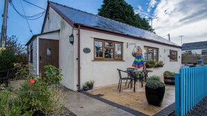 A cottage with a tiled patio, a table and chairs, and potted plants. - Honeysuckle Cottage - 1 Bedroom - Amroth (Narberth)