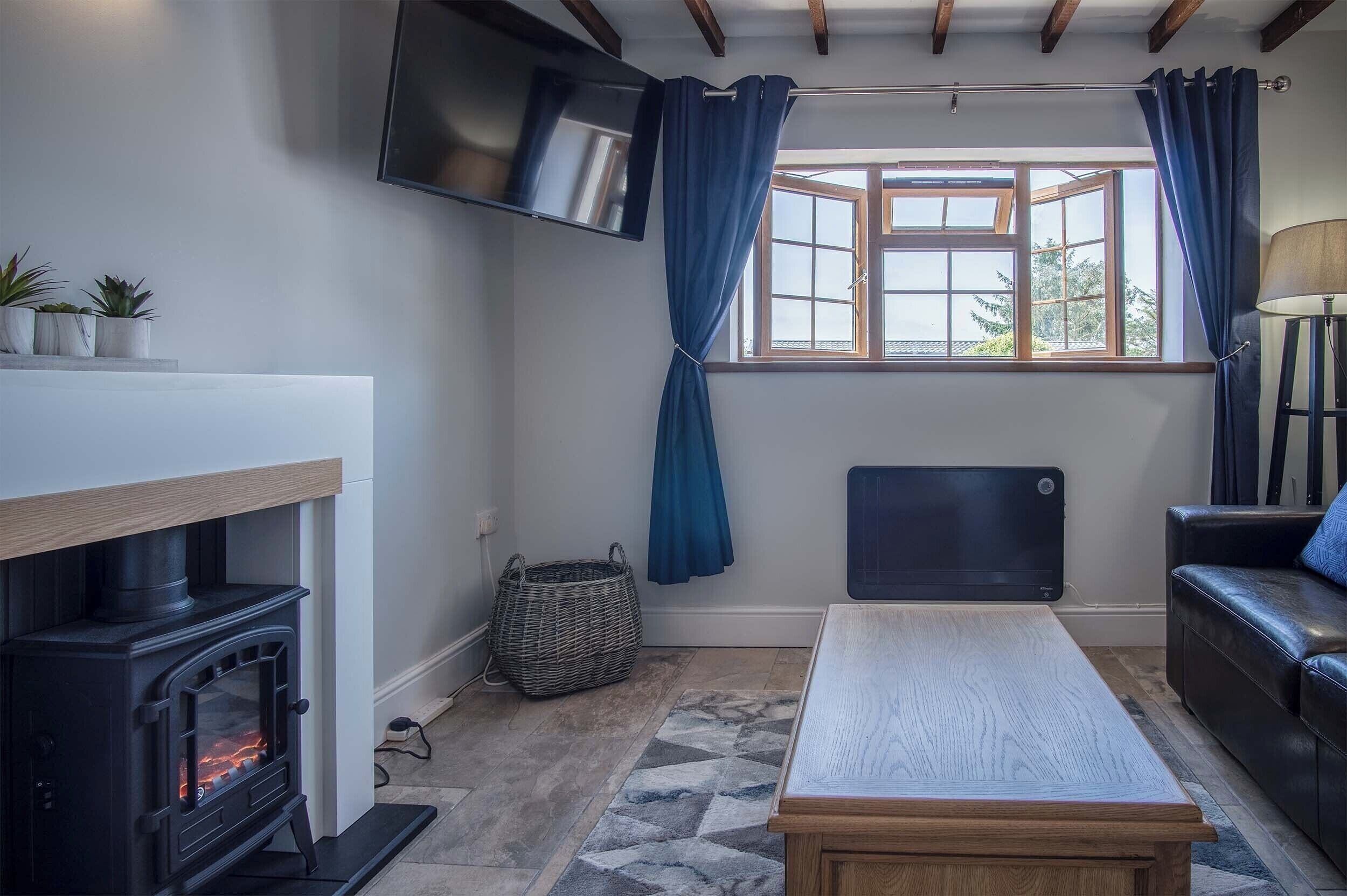 A cozy living room with a fireplace, a television mounted on the wall, a window with curtains, a sofa, and a table.