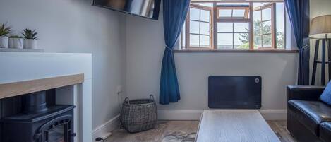 A cozy living room with a fireplace, a television mounted on the wall, a window with curtains, a sofa, and a table.
