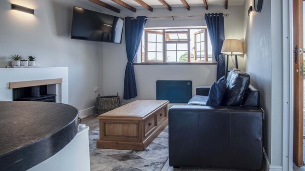 A modern living room with a fireplace, a flat-screen TV, a sofa, and a dining area. - Honeysuckle Cottage - 1 Bedroom - Amroth (Narberth)
