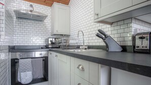 A kitchen with white cabinets, a stainless steel range hood, a toaster, and a knife block. - Honeysuckle Cottage - 1 Bedroom - Amroth (Narberth)