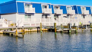 A row of blue and white waterfront cabins with balconies, docked on stilts over water.