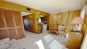 A spacious room with a bed, a dining area with chairs, a kitchen, and a wooden wall.