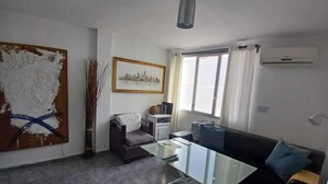 A modern living room with a glass coffee table, a sofa, a chair, a large abstract painting, and a cityscape artwork. - Centrally located apartment in Triana, Seville+swimming pool (Sevilla)
