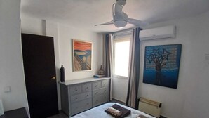 A bedroom with a bed, a dresser, a ceiling fan, and two paintings on the wall. - Centrally located apartment in Triana, Seville+swimming pool (Sevilla)