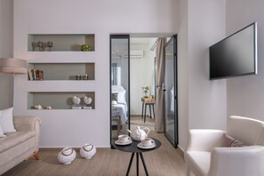 A modern living room with a sofa, a coffee table with teapots, shelves with decorative items, and a TV mounted on the wall.