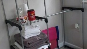 Un lit superposé en métal, avec une étagère en dessous contenant des serviettes pliées, un récipient rouge et un bocal en verre.