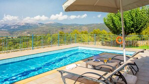 Une piscine dotée de chaises longues et d’un parasol, entourée d’une clôture en métal et offrant une vue sur les montagnes.