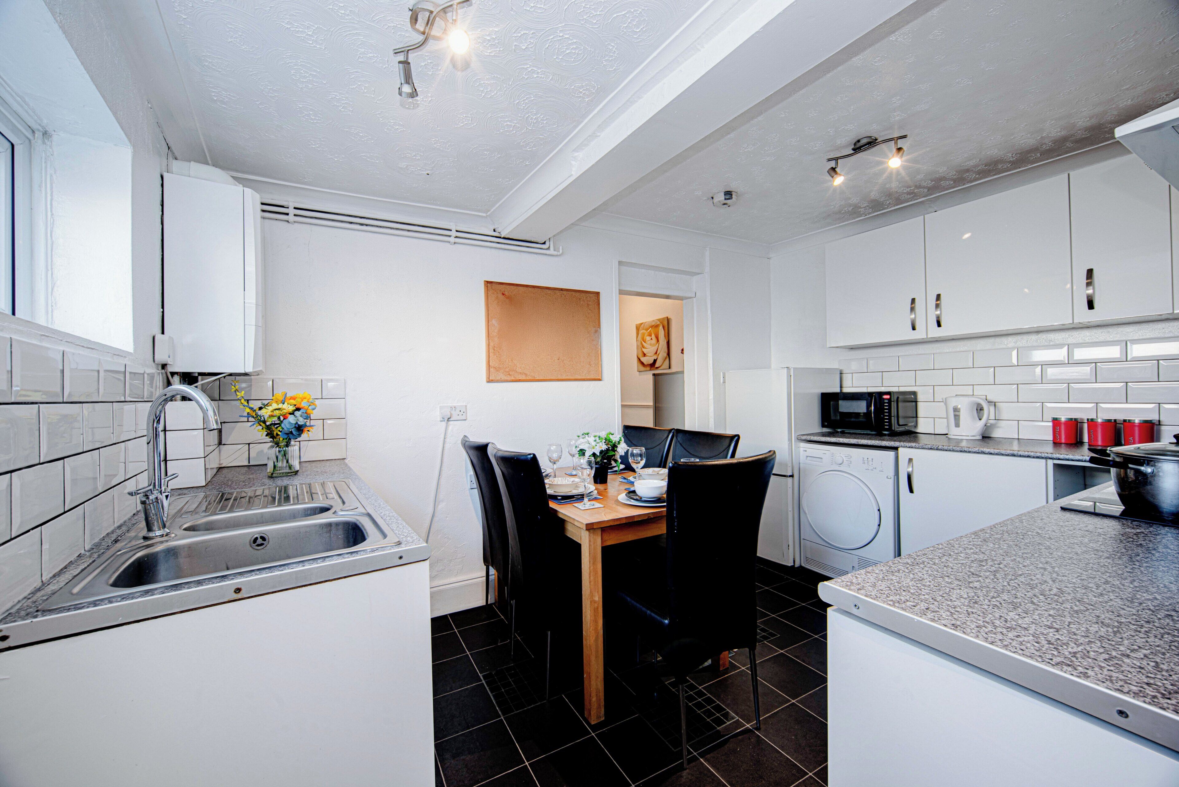 A modern kitchen with a sink, stove, microwave, and a dining area with chairs and a table.