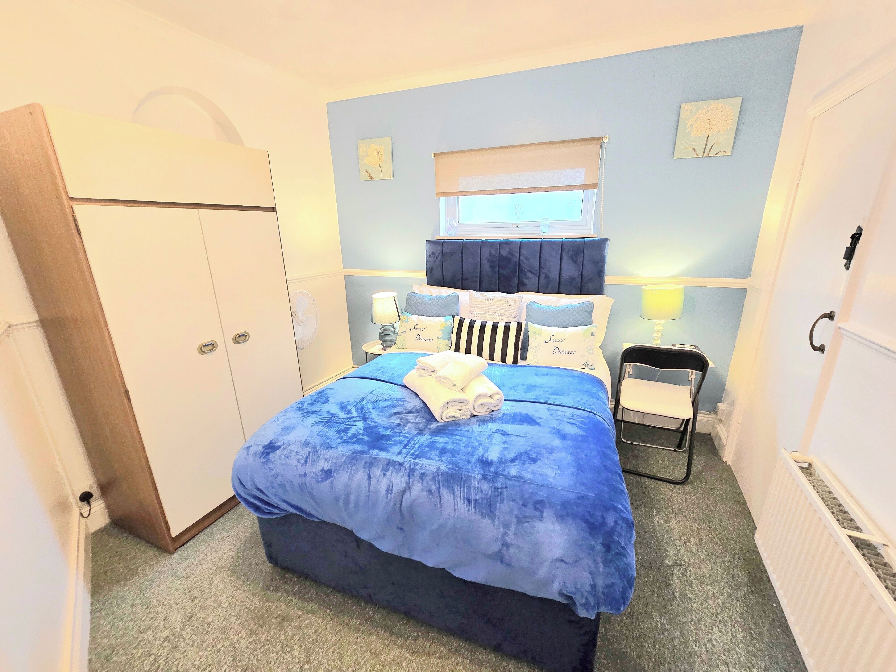 A bedroom with a bed, bedside lamps, a window, a chair, and a wardrobe.