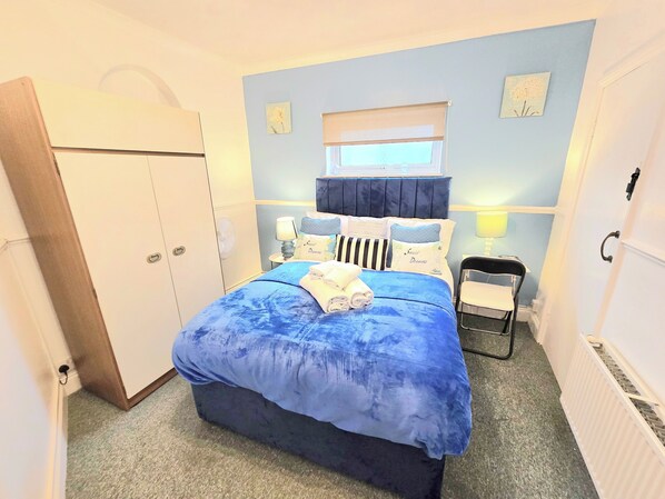 Ein Schlafzimmer mit Bett, Nachttischlampen, einem Fenster, einem Sessel und einem Kleiderschrank.