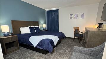 A hotel room with a bed, a desk, a chair, a lamp, and a wall with artwork.