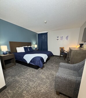 A hotel room with a bed, a desk, a chair, a lamp, and a wall with artwork. - The Northeastland Hotel (Presque Isle)