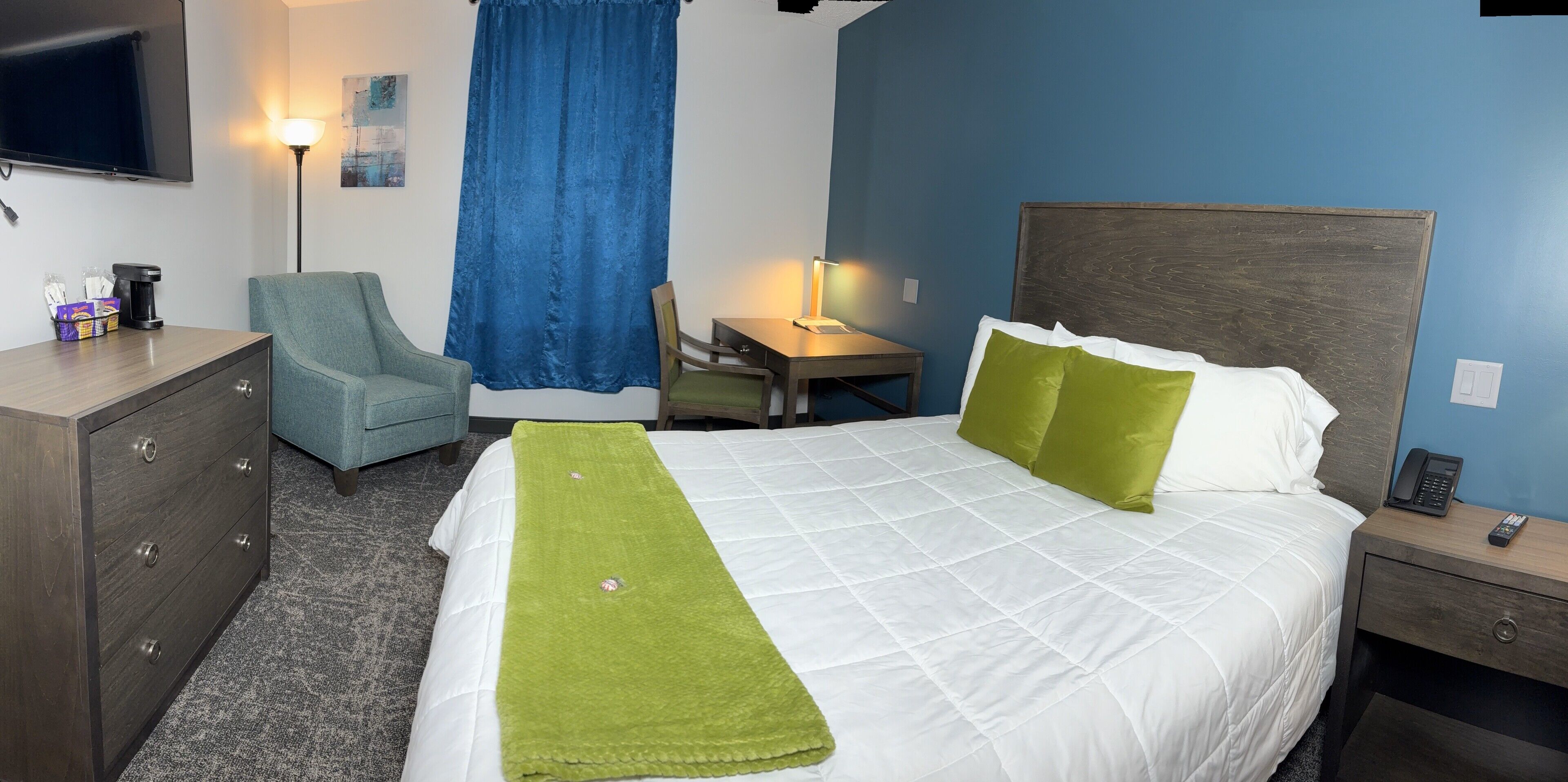 Habitación de hotel con cama, escritorio, silla, cómoda y televisor.