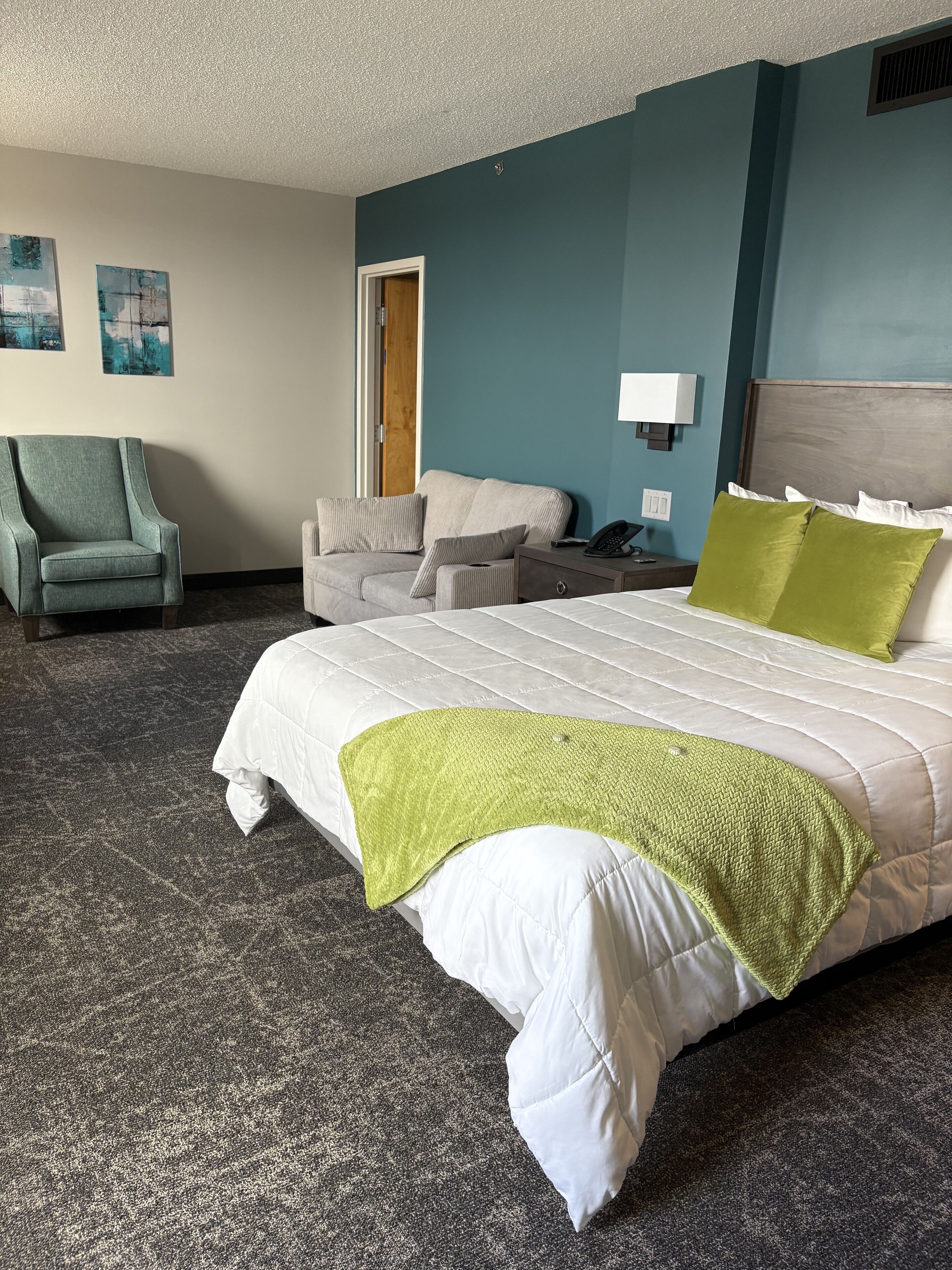 A hotel room with a large bed, a chair, a sofa, a nightstand, and a lamp.