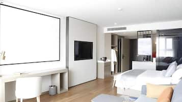 Habitación de hotel moderna con una cama grande, un escritorio con televisor de pantalla plana, un sofá y una pequeña mesa.