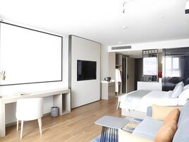 Habitación de hotel moderna con una cama grande, un escritorio con televisor de pantalla plana, un sofá y una pequeña mesa.