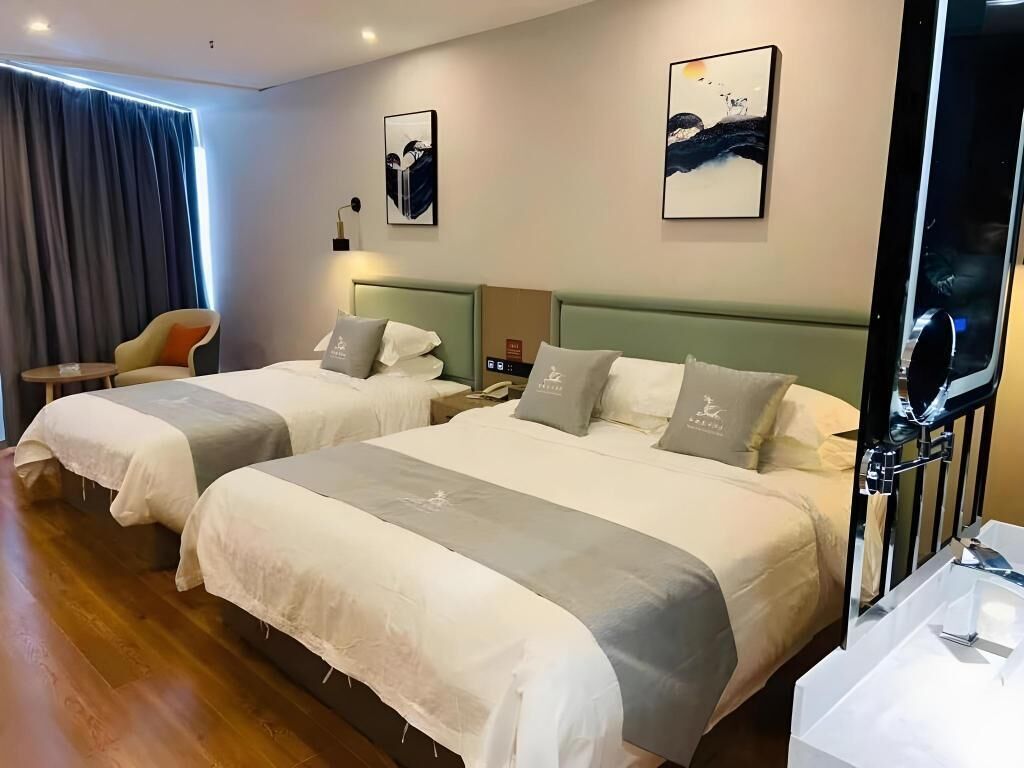 A hotel room with two beds, a chair, a desk, and artwork on the walls.