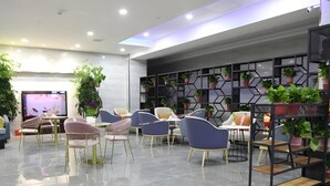 A modern lounge area with seating, a TV, and a wall decorated with plants. - Greentree Eastern Xinjiang Aksu Airport Hotel (Wensu County)