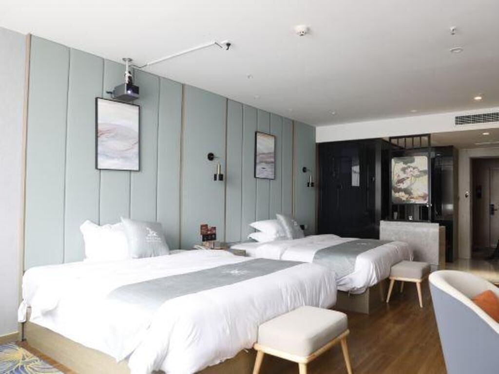 A modern hotel room with two beds, a seating area, and artwork on the walls.
