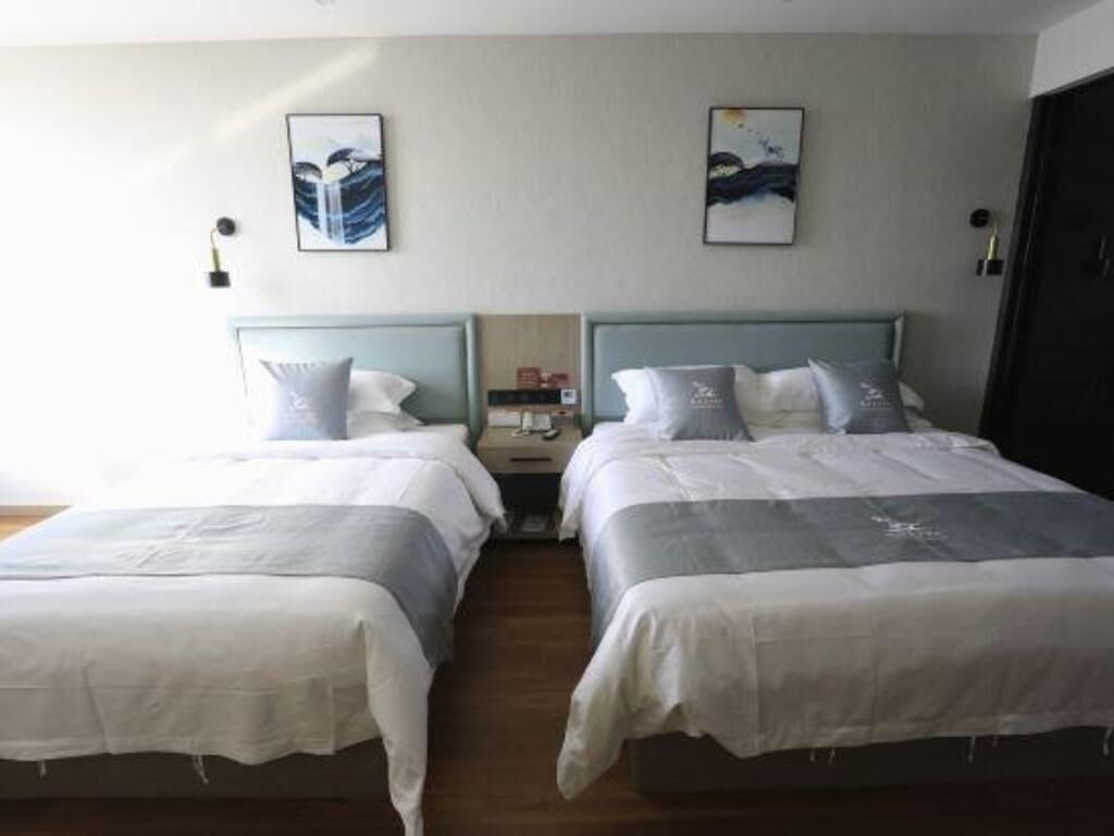 A hotel room with two beds, each with a headboard and pillows. There are wall-mounted lamps and artwork above the beds.