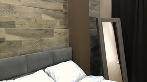 A hotel room with a bed, a headboard, a wall with wooden panels, and a mirror leaning against the wall.