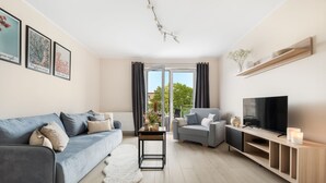 A modern living room with a grey sofa, a grey armchair, a TV, a wooden entertainment unit, and a large window with curtains. - Elite Apartments Mila (Gdansk)