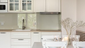 A modern kitchen with white cabinetry, a stainless steel range hood, a window with a view, and a dining area with a table set for two. - Elite Apartments Mila (Gdansk)