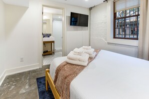 Relax in a serene space with a made bed, wooden chair, and flat-screen TV.