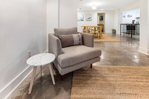 Un salon moderne avec un canapé gris, une petite table ronde et un coin cuisine à l’arrière-plan.