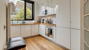 Eine kleine Küche mit weißen Schränken, einer Holz Arbeitsplatte, einem eingebauten Ofen und einem Fenster mit Blick hinaus.