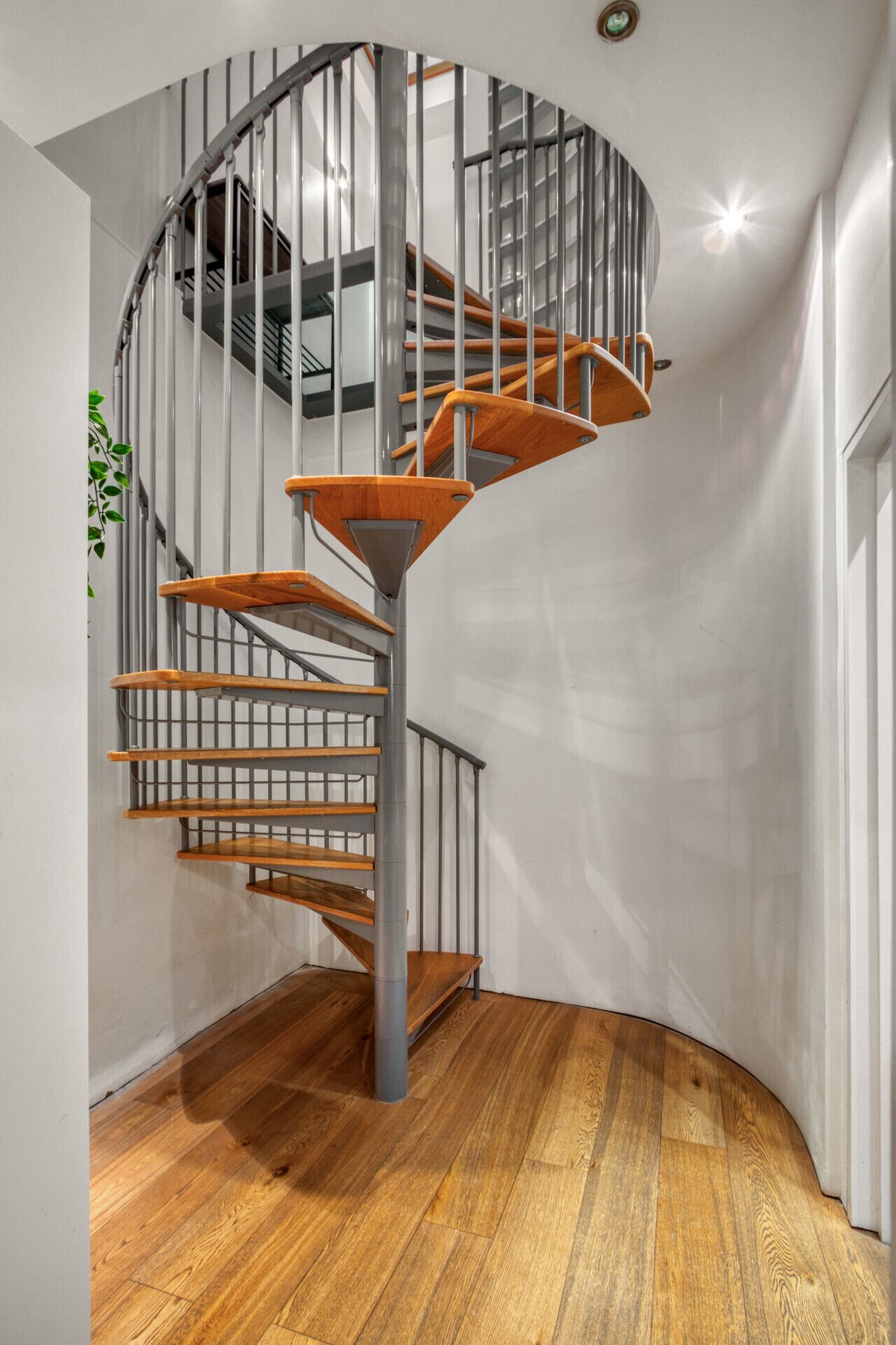 Een moderne spiraaltrap met houten treden en metalen leuningen in een ruimte met een houten vloer en witte wanden.