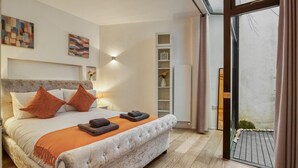 Ein modernes Schlafzimmer mit einem großen Bett, einer eingebauten Sitzbank, einem Nachttisch, einem Wandregal und einer Schiebetür zum Balkon.