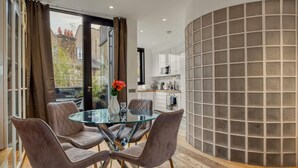 Ein moderner Essbereich mit einem Glastisch, gepolsterten Stühlen und Blick auf die Skyline durch große Fenster.