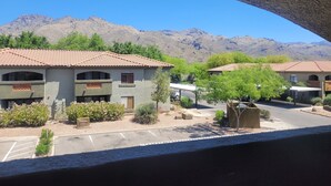 Un edificio de dos pisos con techo de tejas, rodeado de vegetación y montañas al fondo.
