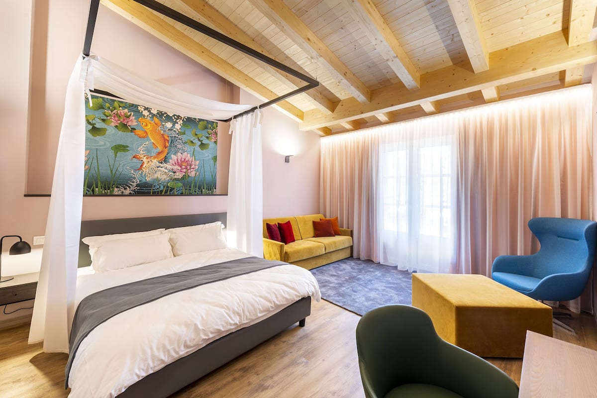 Un dormitorio con una cama, un sofá amarillo, un sillón azul y un cuadro de peces koi.