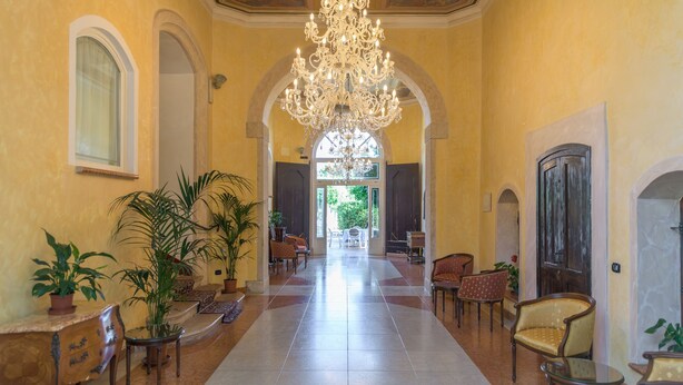 A spacious lobby with a grand chandelier, arched doorways, and comfortable seating areas.
