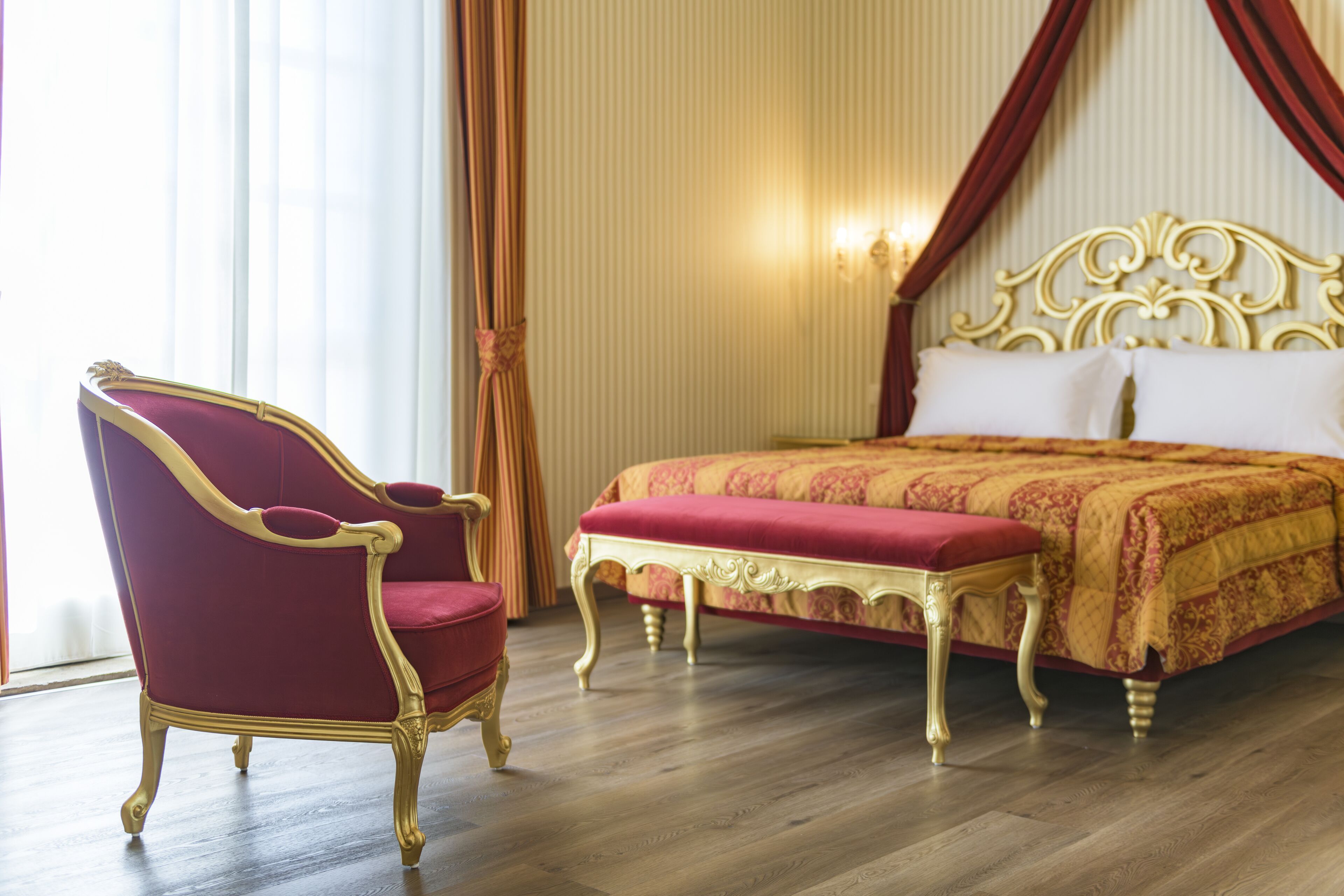 A room with a large bed, a red upholstered chair, and a wooden floor.