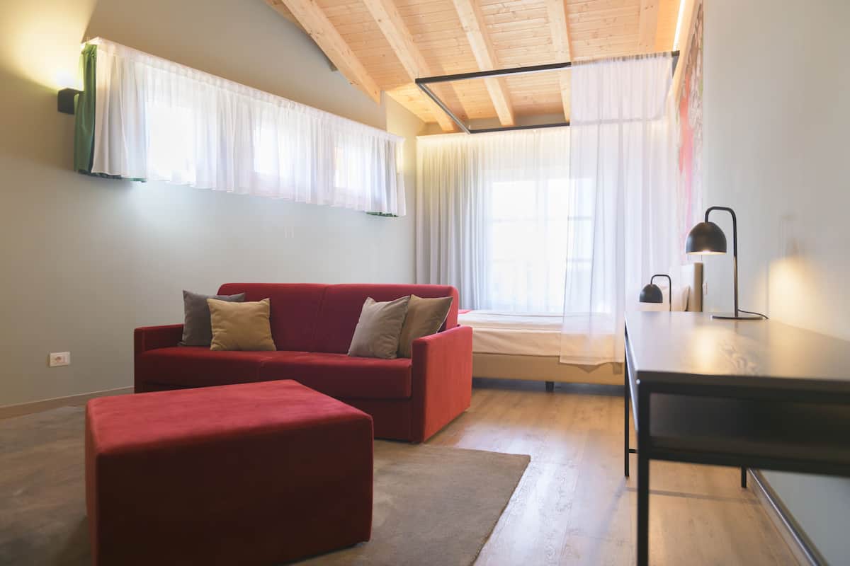Una sala moderna con un sofá rojo, techo de madera y un ventanal con cortinas traslúcidas.