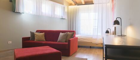 A modern living room with a red sofa, a wooden ceiling, and a large window with sheer curtains.