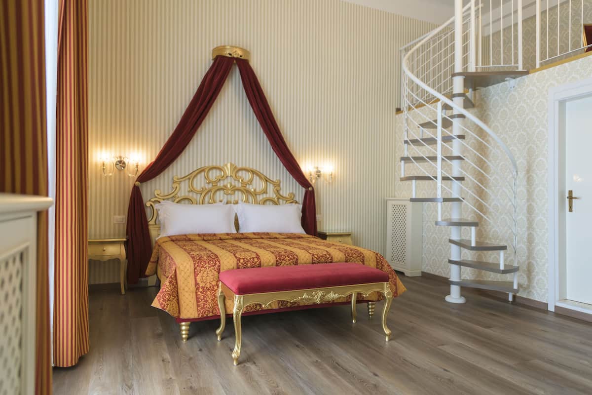 Un dormitorio con cama con dosel, un banco rojo, una escalera en espiral blanca y una pared con rayas verticales.