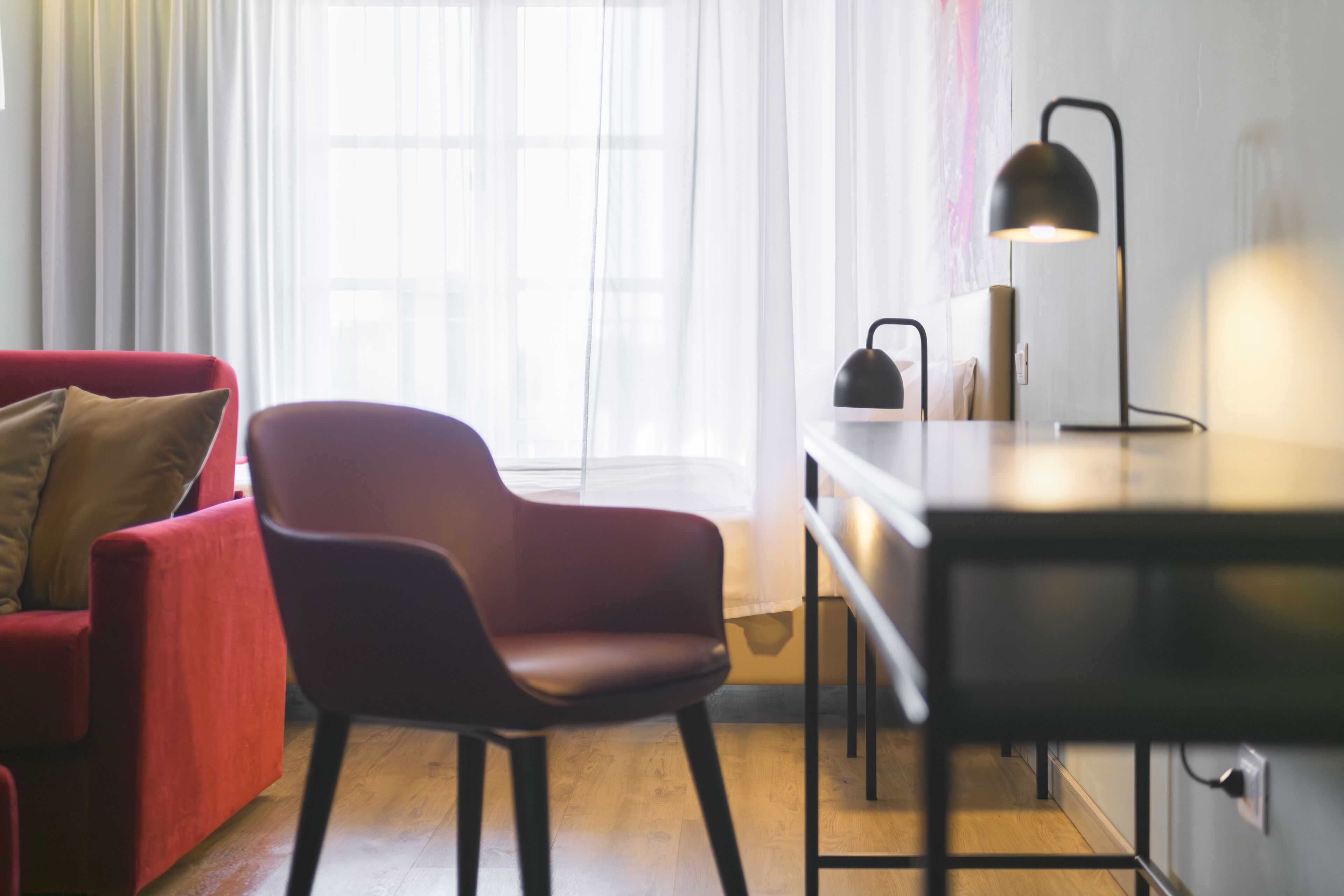 A modern living room with a red sofa, a black chair, and a desk with a lamp.