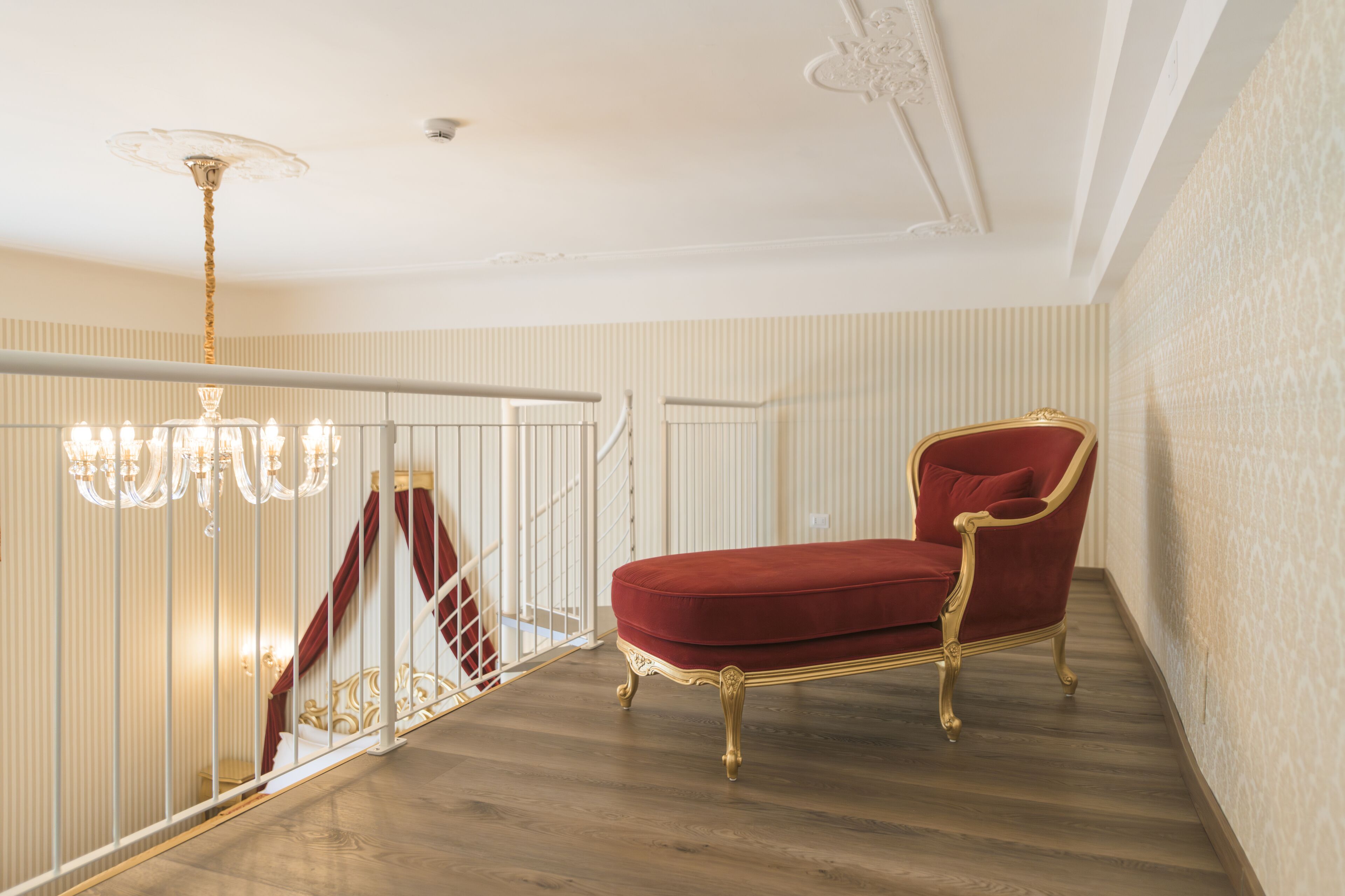 A staircase with a red velvet chair, a chandelier, and a patterned wall.